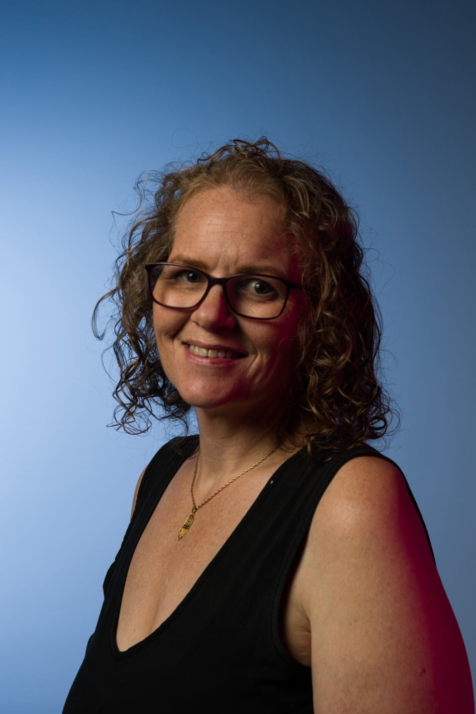 Portrait of artist, Fiona Law with curly hair and glasses, wearing a black top against a blue background